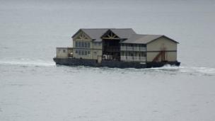 A fishing lodge is being towed across a river