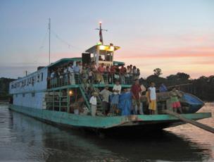 A ferry full of people travels along a river in Amazonian Peru