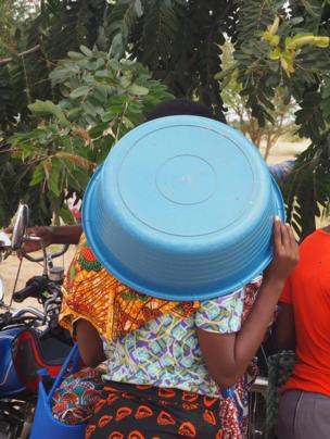 A woman shields her head from the midday sun with a large plastic bowl