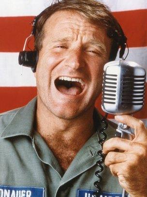 Promotional image of Robin Williams in front of stripes of flag with microphone