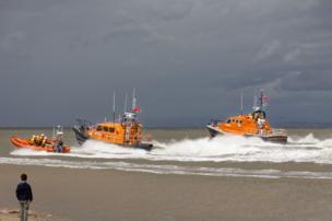 Lifeboats navigate offshore, watched by a young boy
