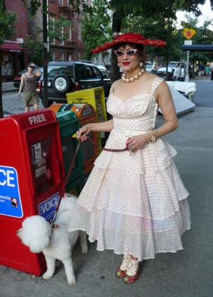 A woman dressed in an 1950s-style polka dot dress walks her dog