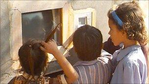 Children using computer via a hole in a wall