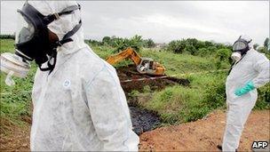 Two civil protection workers pass by a bulldozer clearing a site polluted with toxic waste at the Akouedo district in Abidjan - 19 September 2006