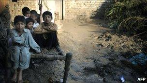 Flood survivors sit on a wooden bed outside their destroyed house in Charsadda