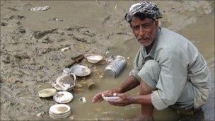 Man washing dishes in flood water. Photo: Owais Barlas
