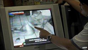 A woman points at the screen as she watches a TV broadcast that includes mobile phone footage of police allegedly torturing a naked man in Manila (18 August 2010)