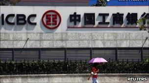 A woman carrying an umbrella walks past an office building that includes a China Telecom office and a branch of the Industrial and Commercial Bank of China in central Beijing