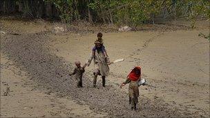 A man wades with his children through flood mud in Nowshera, 20 August, 2010