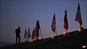 A man stands next to to Chilean flags representing 33 trapped miners outside the San Jose mine in Copiapo, Chile