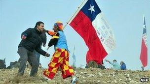 A man in a clown suit holding a Chilean flag celebrates with a TV reporter after one of the drills working to rescue the 33 trapped miners finally reached their shelter in the San Jose mine, near Copiapo, Chile