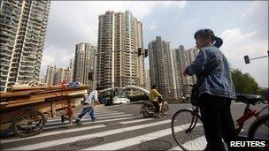 A woman pushes her bikes past a residential development in Shanghai