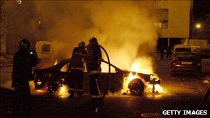 Firefighters try to extinguish a car after rioting in Clichy-sous-Bois (30 October 2005)