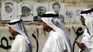 Bahraini men walk by a wall with posters of jailed Shia activists, 22 October