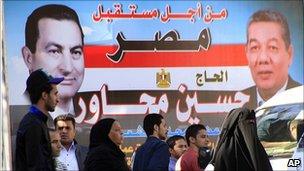 People in Cairo walk in front of election poster featuring President Hosni Mubarak (left) and a ruling NDP candidate