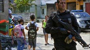 An armed policeman patrols the Complexo do Alemao shantytown in Rio de Janeiro as children walk past