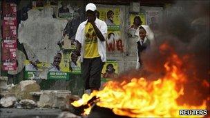 Haitians walk past a burning barricade in Port-au-Prince during protests against the election result