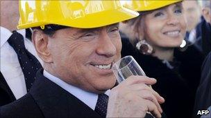 Italian Premier Silvio Berlusconi, wearing a worker's helmet, toasts during the inauguration of work on a new hall for high speed trains at Rome's Tiburtina train station, 10 December 2010