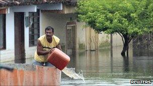 A man removes water from a boat as he moves through flooded streets in La Victoria