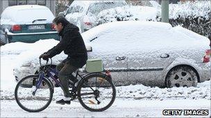 A man rides a bicycle past parked cars covered in ice and snow in Berlin, Germany, 19 December 2010