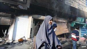 Women walk in front of a burnt mall on 13 January 2011 in a district of Tunis where rioters burnt vehicles and attacked government offices