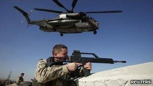 A German soldier keeps watch in Kunduz, Afghanistan, as a helicopter takes off, December 2010