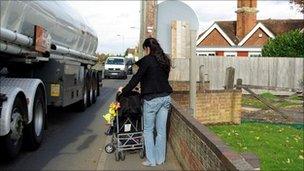 Woman pushing a pushchair on the pavement as a lorry goes past