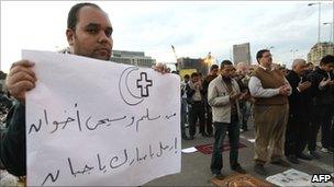A Copt holds a sign as Muslims pray in Tahrir Square, 31 January