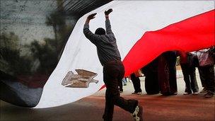 A man runs underneath an Egyptian flag on Tahrir Square (9 Feb 2011)