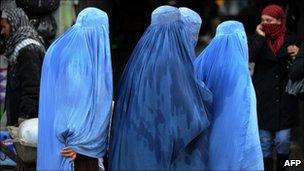 Afghan women wearing burqas walk past shops at a market in Kabul on February 13, 2011