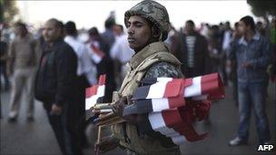 An Egyptian soldier greets demonstrators with national flags as they pour into Cairo's Tahrir Square for celebrations on 18 February 2011