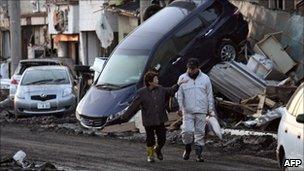 Couple walk past overturned vehicles in Miyako (12 March)