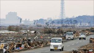Small trucks drive down a road with the Fukushima Daiichi plant in the background