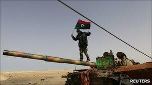 A Libyan rebel fighter walks on a tank near Brega, 6 April 2011.