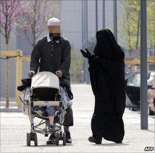 A woman wearing a full Islamic veil walks with a man and a baby's buggy in Venissieux, near Lyon, France, April 2010
