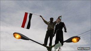 A protester holds a flag and an effigy of Yemeni President Ali Abdullah Saleh while standing on a lamp-post in the Yemeni capital Sanaa, 23 April