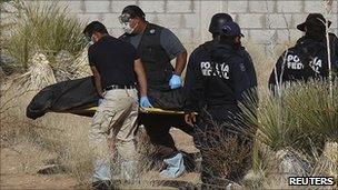 Forensic workers carry the bodies of four men, as federal polices stand guard at a crime scene on the outskirts of Ciudad Juarez, 13 April 2011