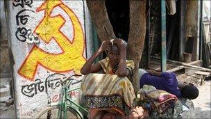 A woman sits under a tree next to a logo of the Communist Party of India (Marxist) in Kolkata in this May 11, 2011 file photo.