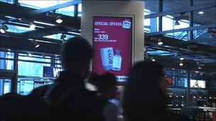 Shoppers walk past a Sony Ziris screen in Oslo Airport's duty free store