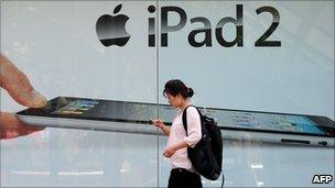 A woman in Bejing checks her cell phone while walking past advertising for the iPad 2.