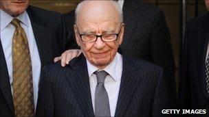 Rupert Murdoch looks down as he leaves a London hotel surrounded by his personal security team