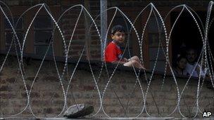 A Kashmiri boy looks through barbed wire set up by Indian policemen in Srinagar, India, on 13 July 2011 after separatists protesting against Indian rule declared a strike