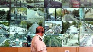 Police officer standing in front of CCTV screens