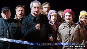 A crowd of people near police tape - London Road production photo by Helen Warner