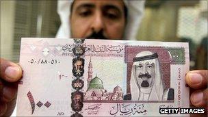 A man holds up a Saudi banknote