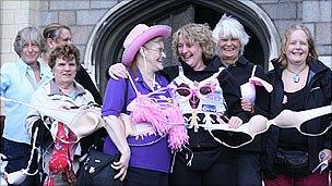 Women stand in front of chain of bras