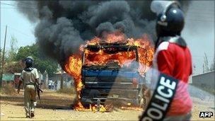 Armed Zambian police officers stand near a burning truck in Lusaka's Kanyama area during election riots Stone-throwing mobs smashed cars and blocked roads during voting, after opposition leader Michael Sata accused President Rupiah Banda's rival camp of rigging the ballot.