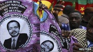 People hold a piece of cloth with pictures of Cameroon"s President Paul Biya, near a street stall at the Carrefour Wada district in the capital Yaounde October 7, 2011.