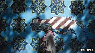 An Iranian woman walks past an anti-US mural on the wall of the former U.S. embassy in Tehran on 12 October 2011