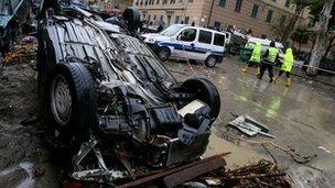 People walk past part of cars and debris in a street of Genoa after heavy rainfall on 5 November 2011